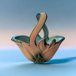 May include: A small, ceramic basket with a pink and green floral design. The basket has a twisted handle and is perfect for holding small items.