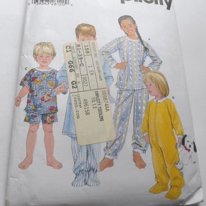 May include: Simplicity sewing pattern for toddlers, featuring three children wearing pajamas. The pattern includes a long-sleeved pajama top and pants, a short-sleeved pajama top and shorts, and a one-piece sleeper. The pattern number is 5874, size AA, and includes instructions for sizes 1/2, 1, and 2.