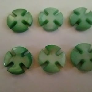 May include: Six green and white plastic buttons with a four-pointed star design. The buttons are round and have a slightly raised center.