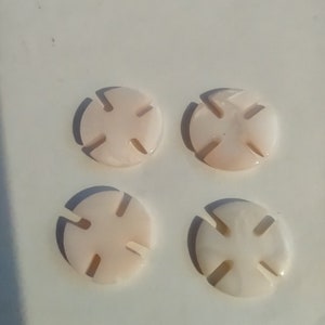 May include: Four white, round, decorative buttons with a cross-shaped design. The buttons have a slightly textured surface.