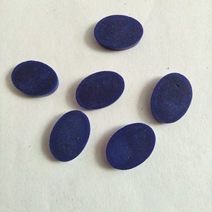 May include: Six oval-shaped, dark blue cabochons, likely lapis lazuli, on a white surface.