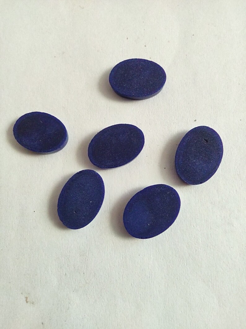 May include: Six oval-shaped, dark blue cabochons, likely lapis lazuli, on a white surface.