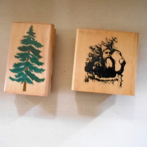 May include: Two wooden rubber stamps, one with a green pine tree design and the other with a black and white illustration of a man with a beard in a forest setting.