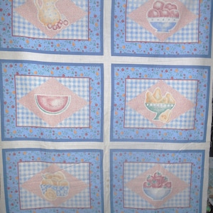 May include: Set of six fabric placemats featuring a harvest theme. Each placemat has a blue and white gingham background with a pink diamond shape in the center. The diamond shapes feature various fruits and vegetables, including a pitcher of cherries, a bowl of red berries, a watermelon, a bowl of peaches, and a bowl of strawberries. The placemats are bordered with a blue and white floral pattern.