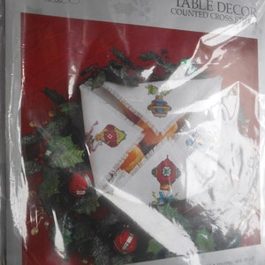 May include: A packaged cross-stitch kit for table decor, featuring a red background and the text "Something Special." The kit includes a bread cover design with old-fashioned ornament patterns. Finished size is 12" x 17".