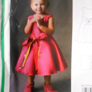 Puede incluir: Una ni&ntilde;a peque&ntilde;a con un vestido rosa brillante con una cinta amarilla y blanca atada alrededor de la cintura. Lleva mocasines rojos con flecos. El vestido es sin mangas y tiene una falda completa.