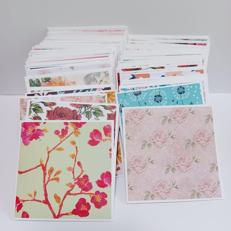 May include: A large stack of square greeting cards featuring a variety of colorful patterns. The front cards display a light green background with bright pink floral branches and a soft pink background with a repeating pattern of pale pink roses.