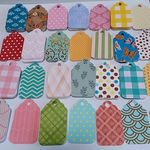 May include: A collection of decorative gift tags in various colors and patterns. Designs include polka dots, floral, geometric, and striped patterns. Each tag has a scalloped edge and a hole for stringing.