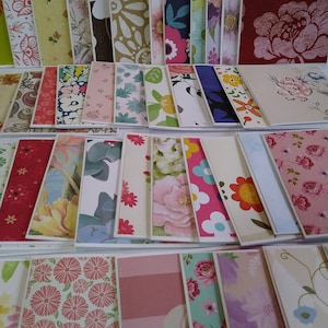 May include: A large collection of rectangular greeting cards featuring a diverse array of printed patterns, including floral motifs, geometric shapes, and botanical designs in various colors such as red, pink, blue, yellow, green, and white.