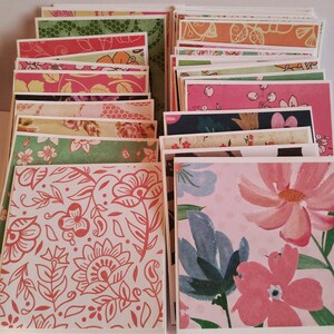 May include: A collection of square greeting cards featuring a variety of colorful patterns, including floral prints, botanical illustrations, and abstract designs in shades of pink, green, orange, blue, and white, stacked in two overlapping rows.