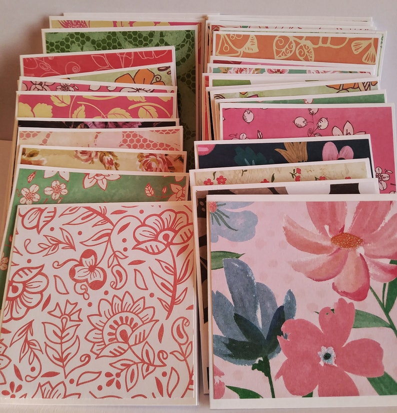 May include: A collection of square greeting cards featuring a variety of colorful patterns, including floral prints, botanical illustrations, and abstract designs in shades of pink, green, orange, blue, and white, stacked in two overlapping rows.