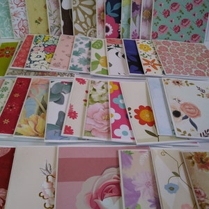 May include: A collection of rectangular greeting cards arranged in rows, featuring a diverse array of printed patterns including floral motifs, geometric shapes, stripes, and botanical illustrations in various colors like pink, blue, green, and yellow.
