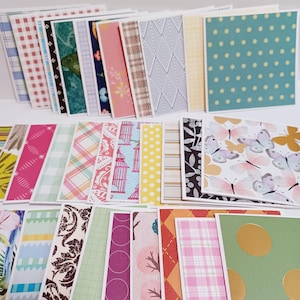 May include: A collection of patterned paper cards in various designs and colors. The cards feature floral, geometric, and polka dot patterns. Some cards have butterfly and birdcage illustrations. The color palette includes pink, blue, green, yellow, and brown.