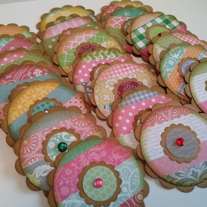 May include: A collection of colorful, scalloped-edge paper embellishments. Each circular piece features a patterned design in shades of pink, green, yellow, and blue, with a brown border and a decorative gem in the center. These are ideal for scrapbooking or crafting.