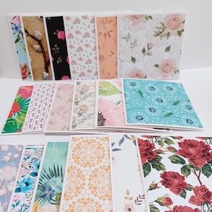 May include: A collection of folded greeting cards featuring a variety of printed patterns including floral designs with red roses, pink blossoms, and blue dandelions, as well as geometric lace motifs, tropical leaves, and botanical illustrations.