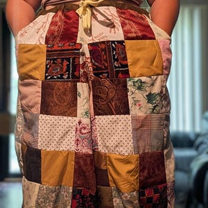 May include: Patchwork trousers featuring a variety of fabric squares in shades of mustard yellow, deep red, brown, and cream. The trousers have a drawstring waist and drawstring cuffs at the bottom, showcasing diverse patterns including paisley, floral, and geometric prints.