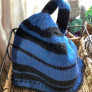May include: A blue and black striped knitted hat with a loop handle. The hat is sitting in a wicker basket.