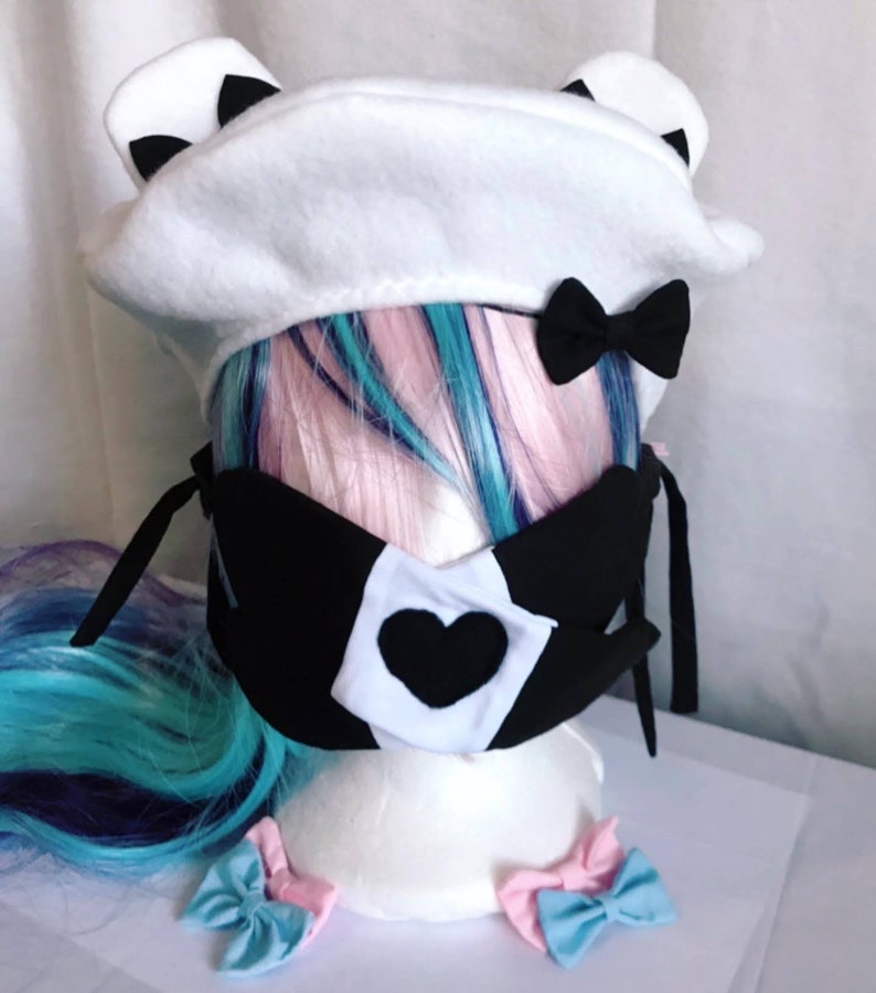 May include: White beret with black ears and a black bow. A black face mask with a white heart and black trim. Two pink and blue bows.