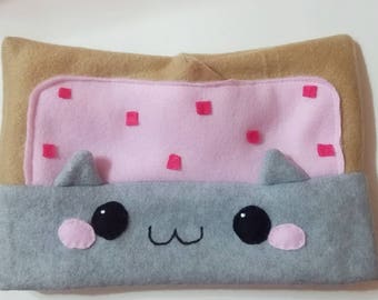 May include: A gray and brown plush pillow shaped like a cat with a pink and brown square on top. The pillow has a cute cartoon face with black eyes and a pink nose.