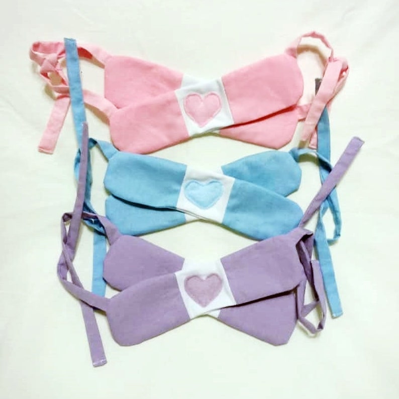 May include: Three fabric bibs with white centers and heart-shaped patches in pink, blue, and purple.