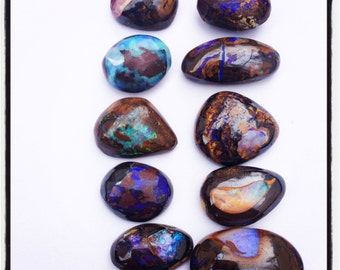 May include: A collection of 10 polished opal stones in various shades of blue, purple, and brown. The stones are arranged in two rows on a white surface.