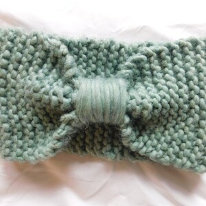 Puede incluir: Una diadema de punto suave de color verde salvia con un detalle de lazo. La diadema está hecha de un hilo grueso y tiene un diseño simple y elegante.