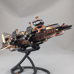 May include: A detailed model of a futuristic airship featuring a metallic copper and black colour scheme. The vessel displays the text EX-028 on its tail fin, multiple cylindrical thrusters, a central cockpit, and various antenna-like projections.