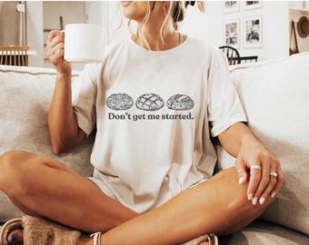 May include: A white t-shirt with a graphic of three different types of bread and the text "Don't get me started."