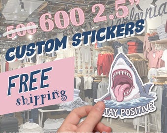 May include: A sticker featuring a cartoon shark with its mouth open and the words "STAY POSITIVE." The image also includes text that reads "500 600 2.5" CUSTOM STICKERS" and "LAMINATED | WATERPROOF & DISHWASHER SAFE."