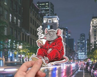 May include: A sticker featuring a cartoon rat in a red tracksuit, smoking a cigar. The rat is wearing red and white sneakers. The background shows a city street at night with buildings and streetlights.