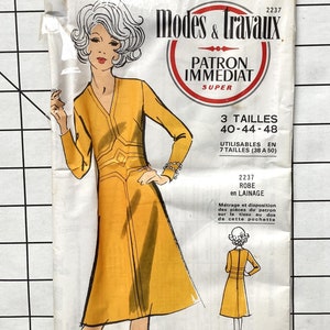 May include: A vintage sewing pattern for a yellow dress with a V-neckline and long sleeves. The pattern is for sizes 40-44-48 and is called "Modes & Travaux Patron Immediat Super 2237 Robe en Lainage".