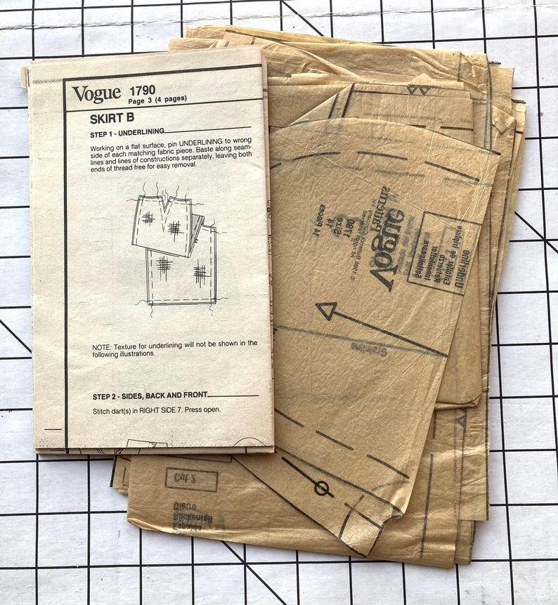 May include: A vintage Vogue sewing pattern for a skirt, pattern number 1790, with instructions for underlining and stitching darts. The pattern is printed on brown paper and includes multiple pieces.