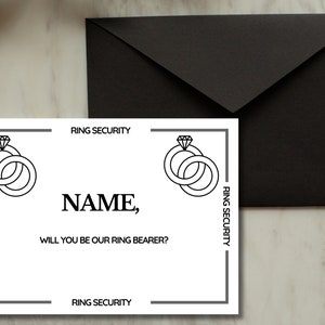 Op de afbeelding: Een witte kaart met zwarte tekst en illustraties. De kaart staat "RING SECURITY" bovenaan en onderaan. In het midden staat "NAME, WILL YOU BE OUR RING BEARER?" met twee illustraties van ringen met diamanten aan beide kanten.