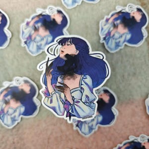 Op de afbeelding: Een sticker met een vrouw met lang blauw haar, die een witte jurk draagt met een donkerblauw en zwart ontwerp. De vrouw kijkt omhoog met haar mond open en haar handen zijn voor haar opgeheven. De sticker heeft een witte rand en de tekst "witchyfoxxi" in de rechterbenedenhoek.