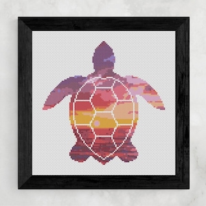 Op de afbeelding: Een ingelijst kruissteekkunstwerk met een silhouet van een zeeschildpad. De schildpad is gevuld met een zonsondergangontwerp in tinten paars, oranje en rood. Het kunstwerk is ingelijst in een zwart houten frame.