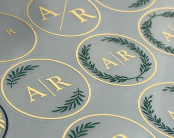May include: A sheet of round stickers with gold lettering and green foliage designs. The stickers feature the initials "A/R" in a gold font.