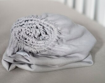 May include: A gray fitted crib sheet made of soft, breathable fabric. The sheet is rolled up and ready to be placed on a crib mattress.
