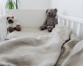 May include: A white crib with a beige linen bedding set. Two stuffed animals, a brown bear and a white sheep, are sitting on the bed.