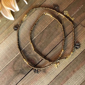 May include: Two gold beaded waist beads with bee charms. The beads are strung on a brown cord and the charms are made of metal.