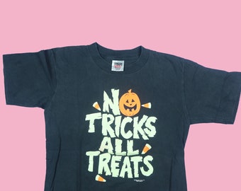 Peut inclure: T-shirt noir avec un motif vert et orange qui dit "No Tricks All Treats" avec un visage de citrouille au milieu.