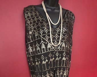May include: A black sleeveless dress with a gold geometric pattern. The dress has a V-neckline and a beaded necklace.