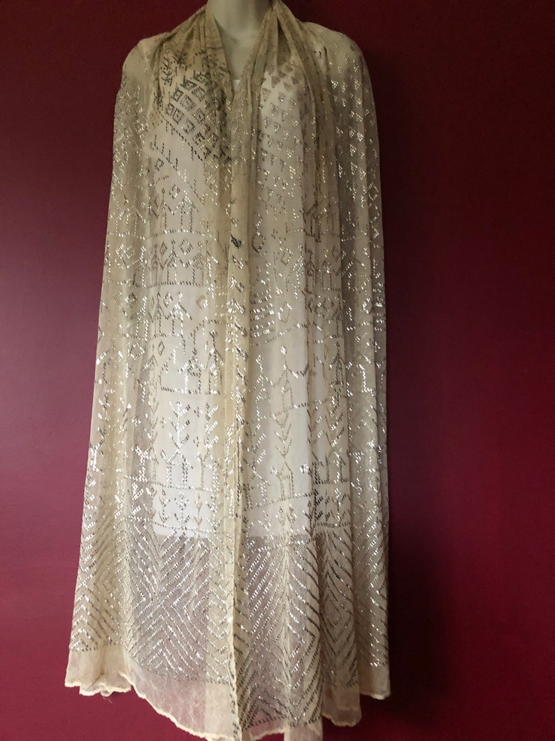 Pu&ograve; includere: Un scialle bianco in chiffon con un motivo geometrico argentato. Lo scialle &egrave; decorato con perline e ha una texture delicata e fluida.