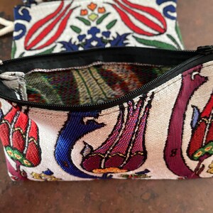 Puede incluir: Una peque&ntilde;a bolsa blanca con cremallera negra. La bolsa est&aacute; decorada con un estampado floral colorido con tulipanes rojos, azules y morados. El estampado recuerda a los textiles turcos tradicionales.
