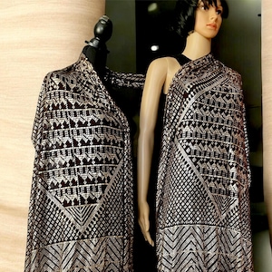 Puede incluir: Un chal marrón oscuro con un patrón geométrico plateado se muestra en un maniquí. El diseño incluye triángulos y rombos. El maniquí lleva una camiseta negra. Un accesorio elegante.