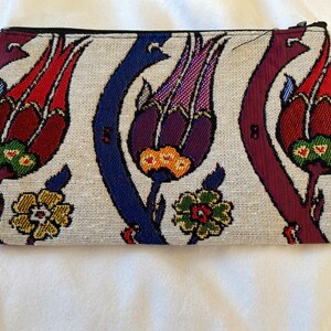 Puede incluir: Una bolsa blanca con cremallera con un estampado floral colorido. El estampado presenta flores rojas, moradas, azules, verdes y amarillas sobre un fondo blanco.