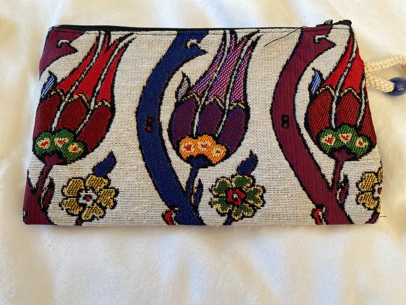 Puede incluir: Una bolsa blanca con cremallera con un estampado floral colorido. El estampado presenta flores rojas, moradas, azules, verdes y amarillas sobre un fondo blanco.