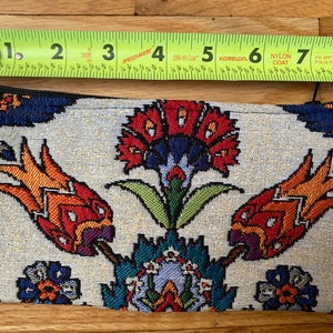 Puede incluir: Una bolsa blanca con cremallera con un estampado floral colorido. El estampado presenta flores rojas, naranjas, amarillas, verdes, azules y moradas sobre un fondo blanco.