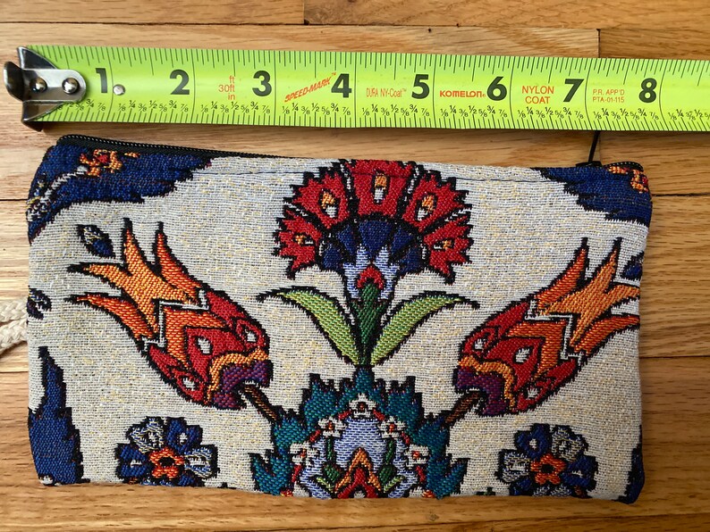 Puede incluir: Una bolsa blanca con cremallera con un estampado floral colorido. El estampado presenta flores rojas, naranjas, amarillas, verdes, azules y moradas sobre un fondo blanco.