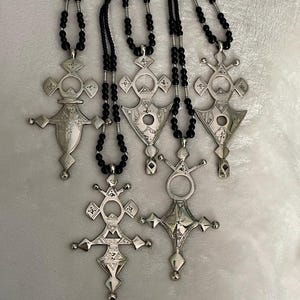 May include: Five silver pendant necklaces with detailed cross designs. Each pendant hangs from a black beaded chain. The crosses display geometric patterns and decorative elements, suggesting a vintage or tribal style.