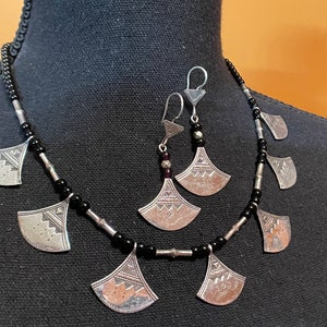 May include: A silver necklace with black beads and silver pendant charms in the shape of a fan. Matching silver earrings with black beads and fan-shaped charms.